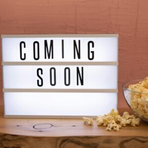 Lightbox sign displaying 'Coming Soon' next to a bowl of popcorn on wooden surface.