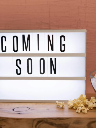 Lightbox sign displaying 'Coming Soon' next to a bowl of popcorn on wooden surface.