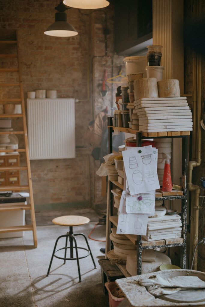 A warm, rustic ceramic workshop featuring pottery tools, shelves, and sketched designs on a table.